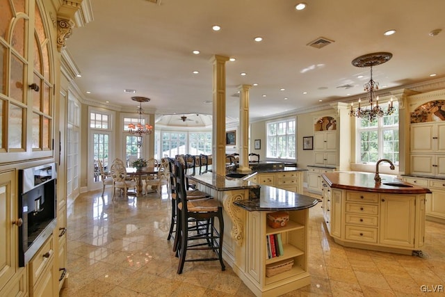 kitchen with a center island with sink, pendant lighting, crown molding, and decorative columns