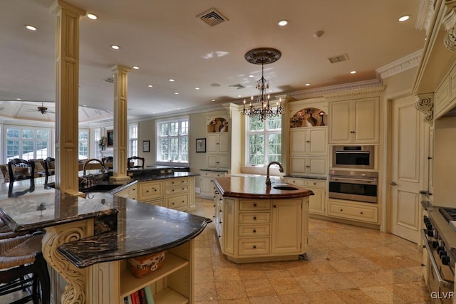 kitchen featuring decorative columns, kitchen peninsula, cream cabinets, pendant lighting, and a center island with sink