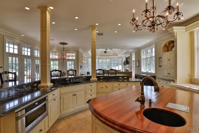 kitchen featuring cream cabinets, crown molding, sink, hanging light fixtures, and decorative columns