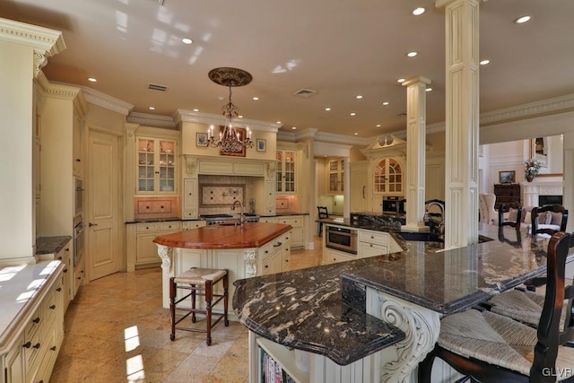 kitchen with a kitchen breakfast bar, decorative columns, ornamental molding, a large island with sink, and dark stone countertops