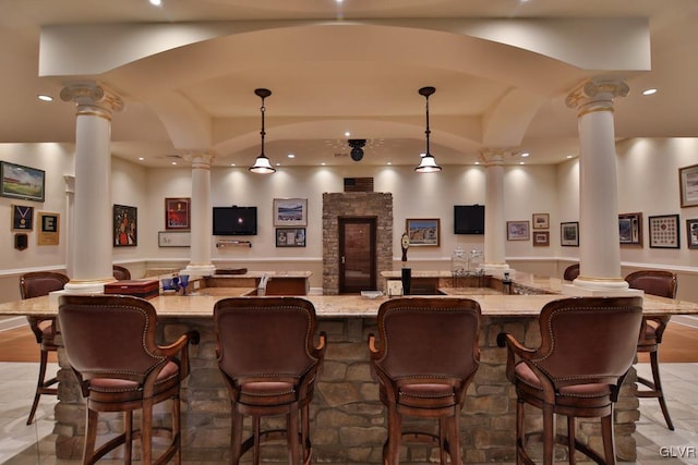 bar with light stone countertops, hanging light fixtures, and decorative columns