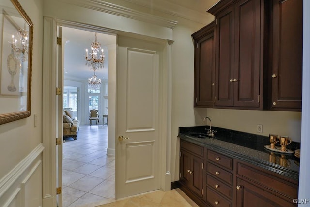 bar featuring dark stone counters, crown molding, sink, light tile patterned floors, and a chandelier