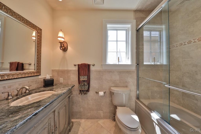 full bathroom with tile patterned flooring, enclosed tub / shower combo, toilet, vanity, and tile walls