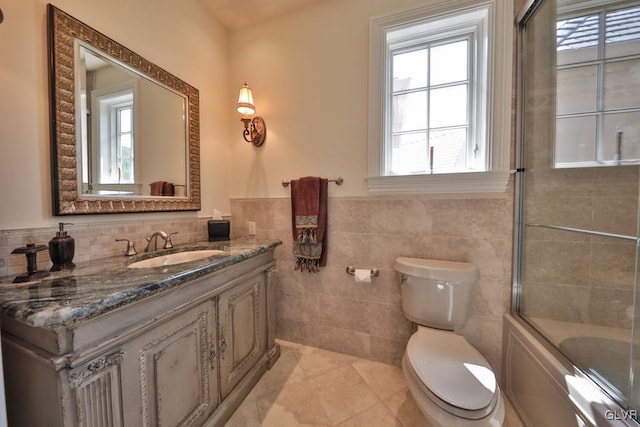 full bathroom with combined bath / shower with glass door, tile patterned floors, vanity, tile walls, and toilet