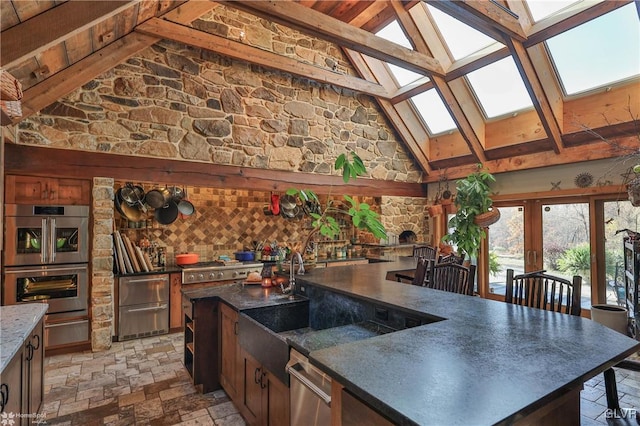 kitchen featuring beam ceiling, an island with sink, a skylight, sink, and stainless steel double oven