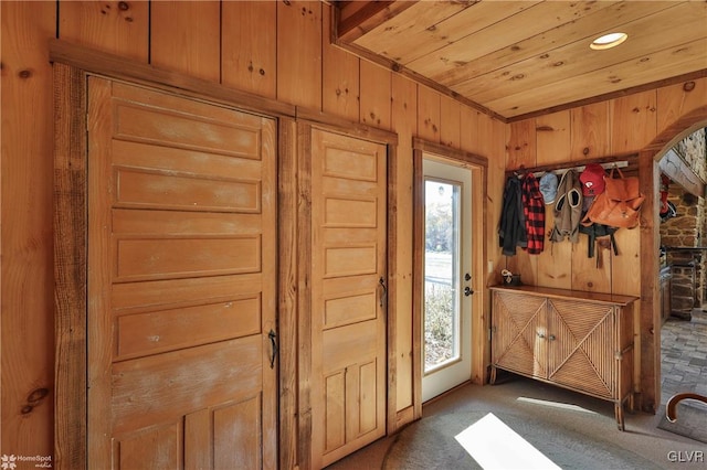 doorway to outside with wooden walls and carpet flooring