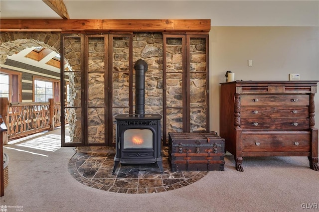 interior details featuring a wood stove, beamed ceiling, and carpet