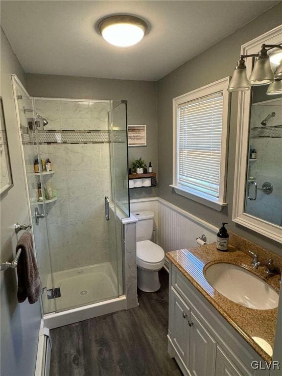 bathroom with hardwood / wood-style floors, a baseboard radiator, a shower with door, toilet, and vanity