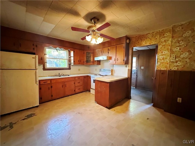 kitchen featuring kitchen peninsula, ceiling fan, wood walls, sink, and white appliances