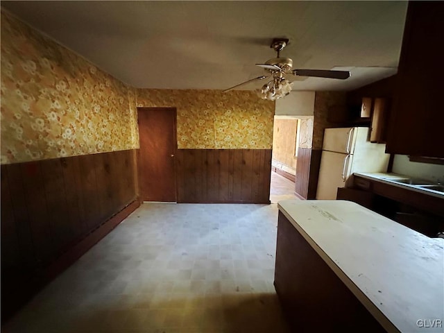 kitchen with ceiling fan, sink, wooden walls, and white refrigerator