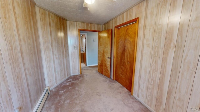 hallway with light carpet, wood walls, and a baseboard radiator