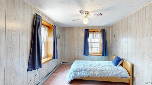 bedroom featuring a baseboard heating unit, carpet floors, wooden walls, and ceiling fan