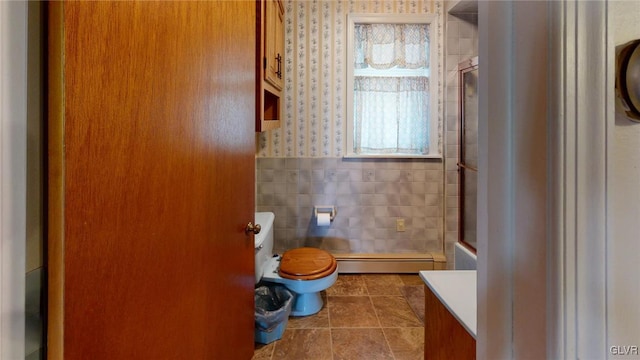 bathroom featuring a baseboard heating unit, walk in shower, tile walls, toilet, and vanity