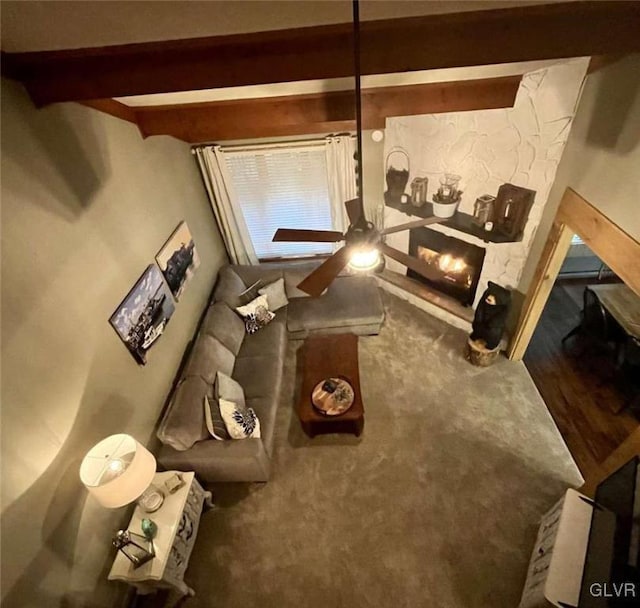 living room featuring beamed ceiling, carpet flooring, and a stone fireplace