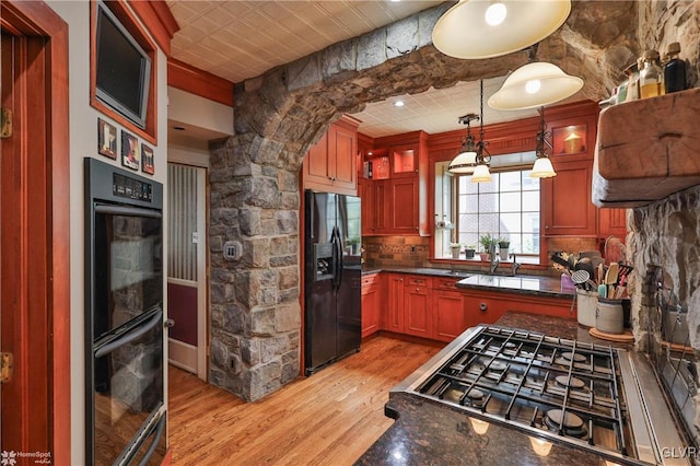 kitchen with black appliances, tasteful backsplash, pendant lighting, light hardwood / wood-style flooring, and dark stone countertops