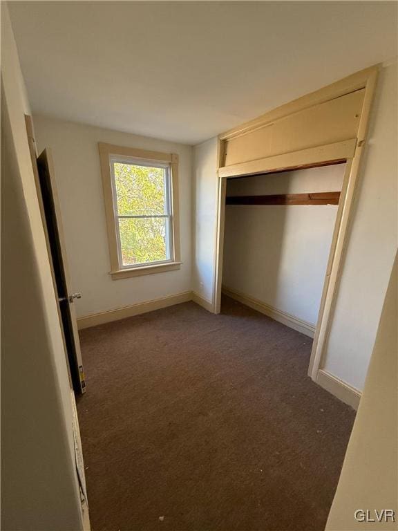 unfurnished bedroom with dark carpet and a closet