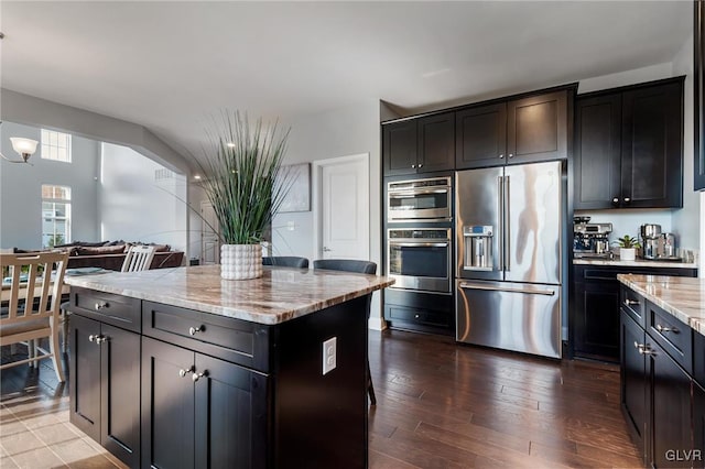 kitchen with stainless steel appliances, light stone countertops, dark hardwood / wood-style floors, and a center island