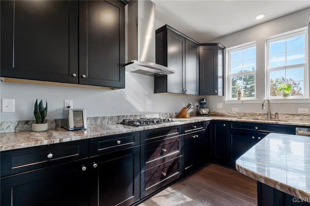 kitchen featuring dark wood-type flooring, light stone counters, stainless steel gas cooktop, sink, and wall chimney range hood