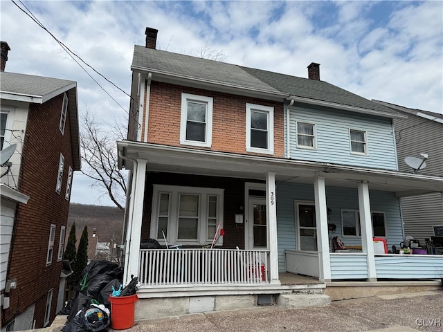 view of front of property with a porch, brick siding, roof with shingles, and a chimney