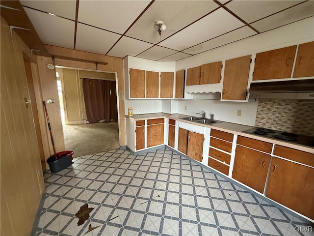 kitchen with brown cabinetry, light floors, a sink, light countertops, and wood walls