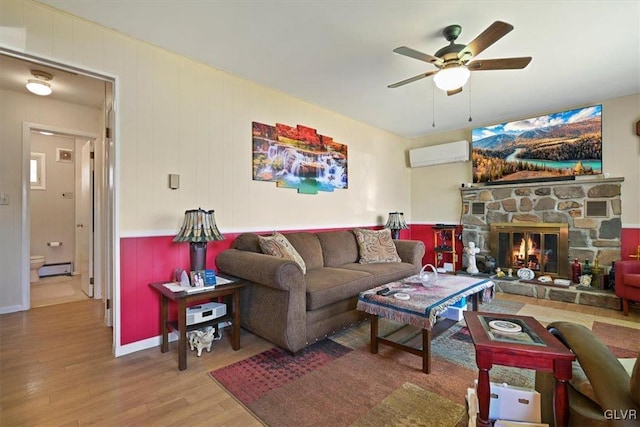 living room featuring a wall mounted AC, a fireplace, hardwood / wood-style floors, baseboard heating, and ceiling fan