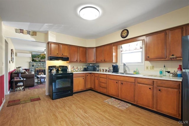 kitchen with black appliances, a fireplace, sink, a wall mounted air conditioner, and light hardwood / wood-style floors