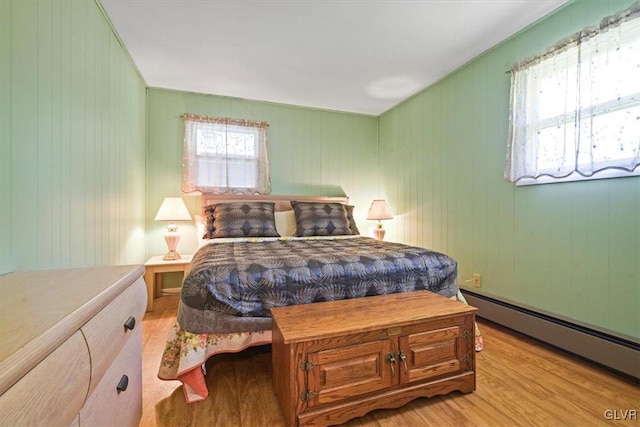 bedroom with wood walls, baseboard heating, and light hardwood / wood-style floors