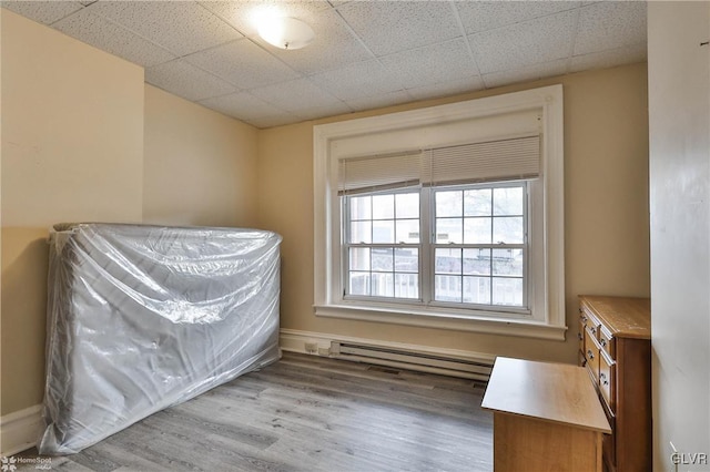 bedroom featuring a paneled ceiling, wood-type flooring, and a baseboard heating unit