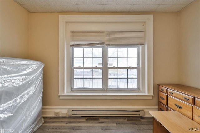 bedroom featuring dark hardwood / wood-style floors, a baseboard heating unit, and a drop ceiling