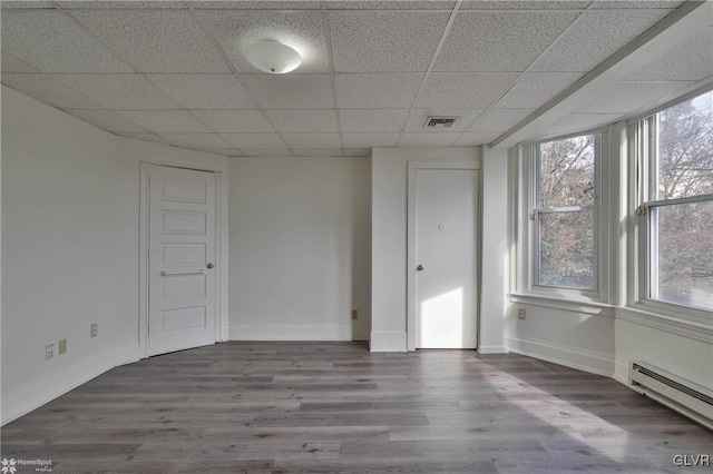 empty room featuring baseboard heating, hardwood / wood-style floors, a wealth of natural light, and a drop ceiling