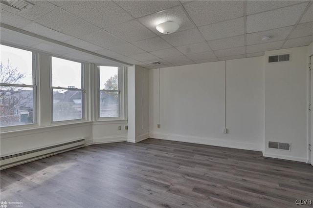 empty room with baseboard heating, hardwood / wood-style floors, and a paneled ceiling