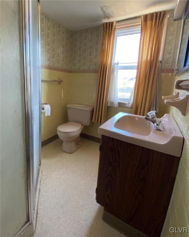 bathroom featuring tile walls, vanity, toilet, and a shower with shower door