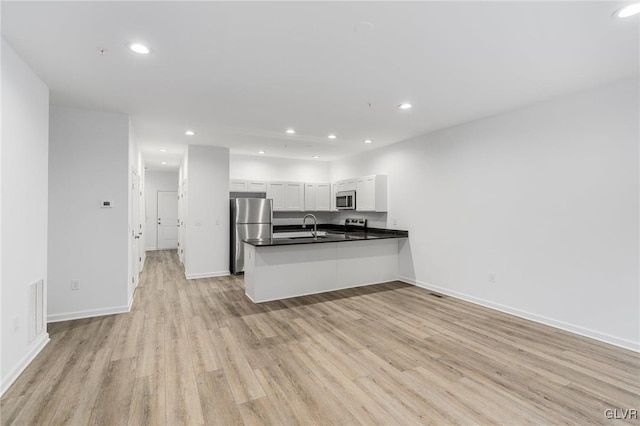 kitchen with stainless steel appliances, white cabinets, kitchen peninsula, sink, and light hardwood / wood-style flooring