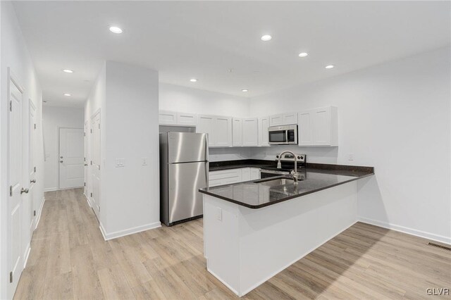 kitchen featuring stainless steel appliances, white cabinets, kitchen peninsula, sink, and light wood-type flooring