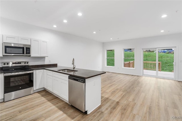 kitchen with dark countertops, light wood-style flooring, a peninsula, stainless steel appliances, and a sink