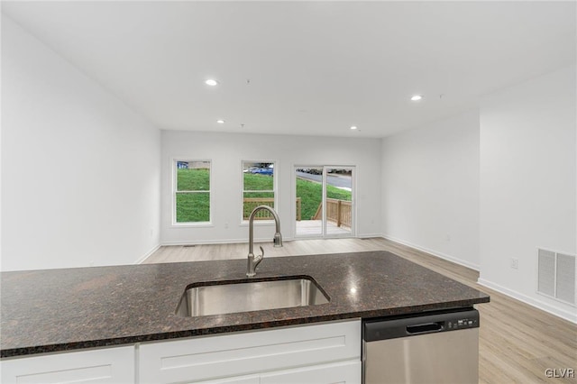 kitchen featuring visible vents, stainless steel dishwasher, dark stone counters, a sink, and light wood-type flooring