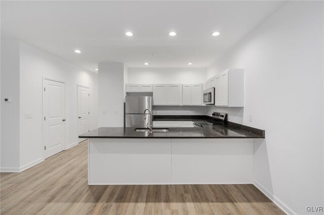 kitchen with white cabinets, kitchen peninsula, appliances with stainless steel finishes, and light hardwood / wood-style flooring