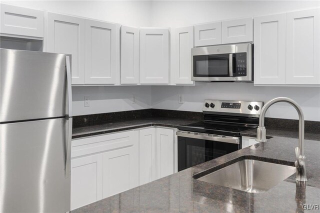 kitchen with dark stone countertops, white cabinetry, appliances with stainless steel finishes, and sink