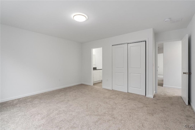 unfurnished bedroom featuring ensuite bathroom, light colored carpet, and a closet