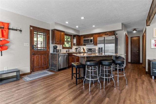 kitchen featuring light stone countertops, a kitchen island, dark hardwood / wood-style flooring, stainless steel appliances, and a kitchen breakfast bar