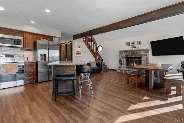 kitchen with backsplash, a fireplace, light stone countertops, a breakfast bar area, and stainless steel appliances