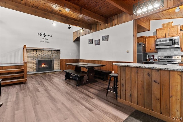 kitchen with a fireplace, light wood-type flooring, appliances with stainless steel finishes, wood ceiling, and a breakfast bar area