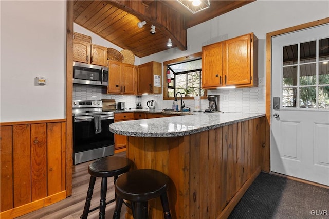 kitchen with lofted ceiling, kitchen peninsula, sink, a kitchen breakfast bar, and stainless steel appliances