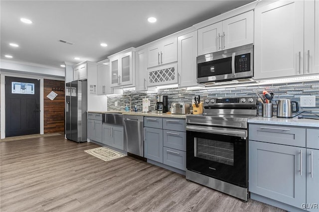 kitchen with appliances with stainless steel finishes, white cabinetry, decorative backsplash, light hardwood / wood-style floors, and gray cabinets