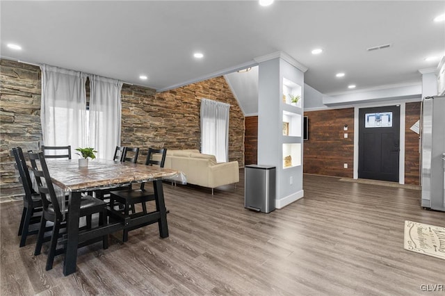 dining area featuring wood-type flooring, wooden walls, and ornamental molding