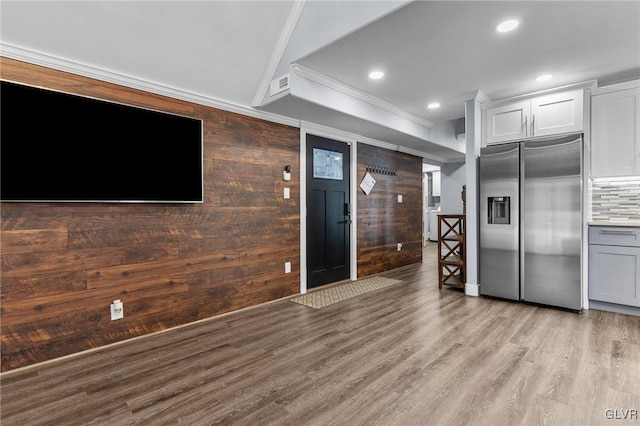 kitchen with white cabinets, wooden walls, decorative backsplash, stainless steel fridge, and ornamental molding