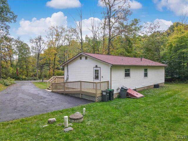 view of property exterior with aphalt driveway, a lawn, a forest view, and a deck