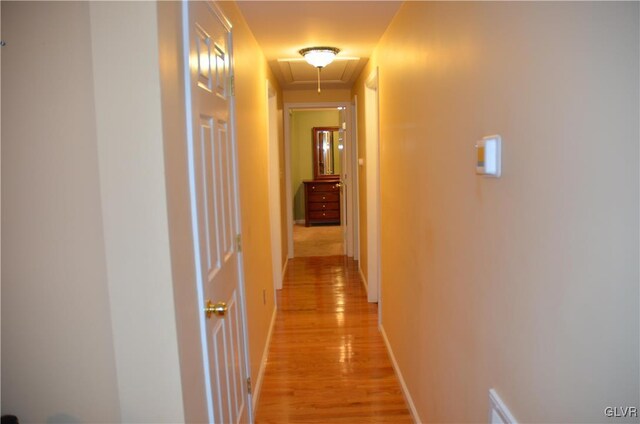 corridor with baseboards, attic access, and light wood finished floors