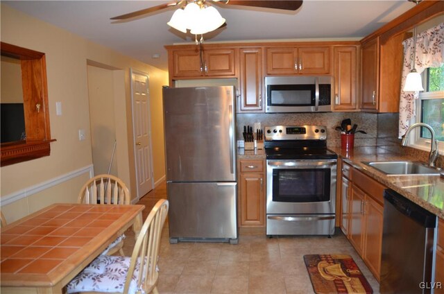 kitchen featuring a ceiling fan, a sink, backsplash, stainless steel appliances, and brown cabinetry