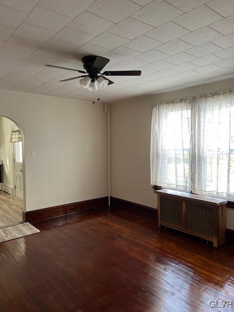 empty room featuring radiator heating unit, dark wood-type flooring, and ceiling fan